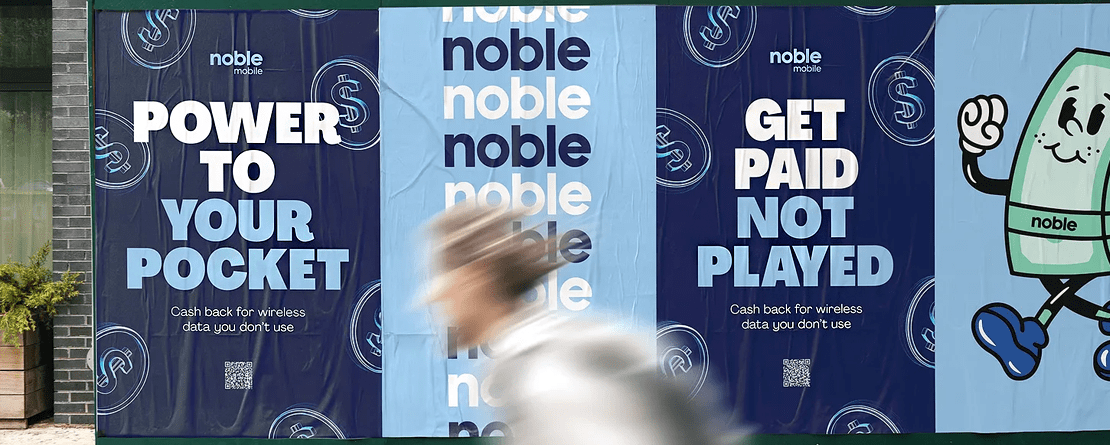 A person walking past posters from the MVNO Noble Mobile
