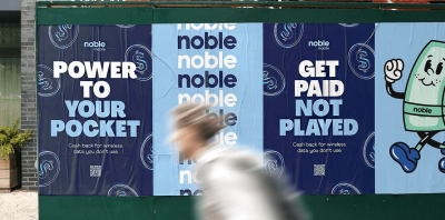 A person walking past posters from the MVNO Noble Mobile