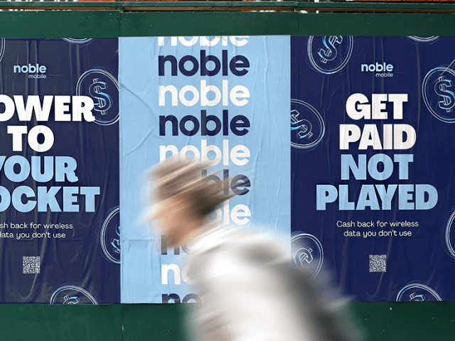 A person walking past posters from the MVNO Noble Mobile